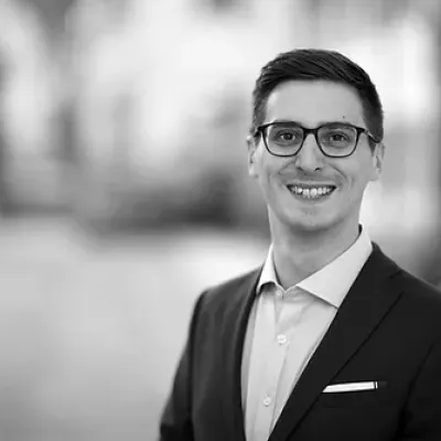 Young man in suit jacket wearing glasses smiles at camera.