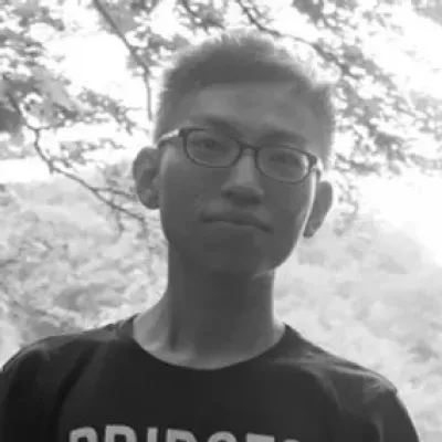 Young man with glasses stands under a tree and smiles at the camera.